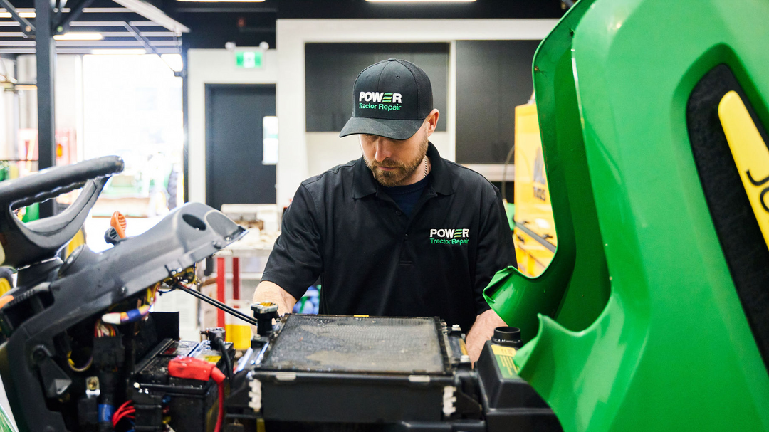 Person working on a green John Deere lawn mower in a workshop.