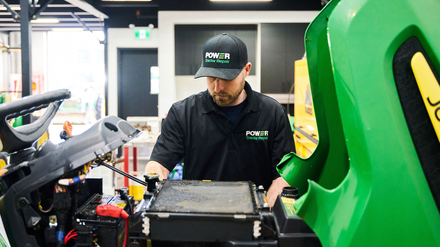 Person working on a green John Deere lawn mower in a workshop.