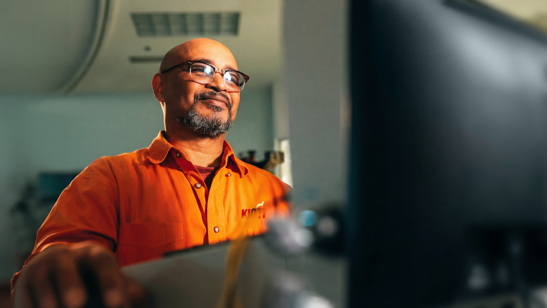 Man in orange shirt using a tablet in an industrial setting